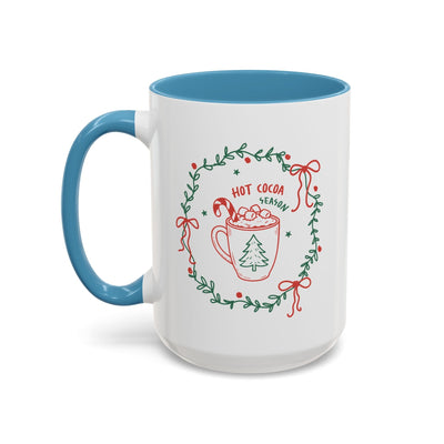 White ceramic mug with blue handle and interior, festive hot cocoa season design with greenery and red accents