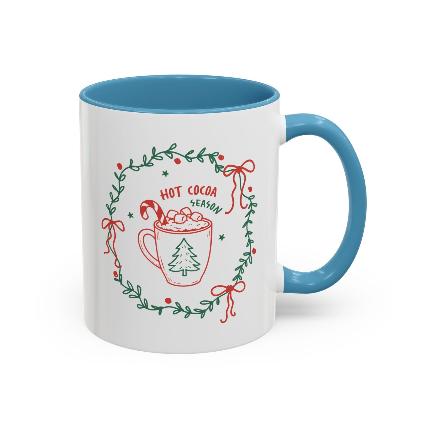 Ceramic mug with blue handle and interior featuring hot cocoa season design with greenery wreath