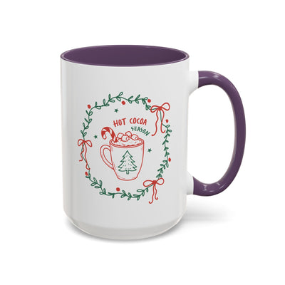 white ceramic mug with purple handle and interior featuring hot cocoa season design with greenery wreath and festive red accents