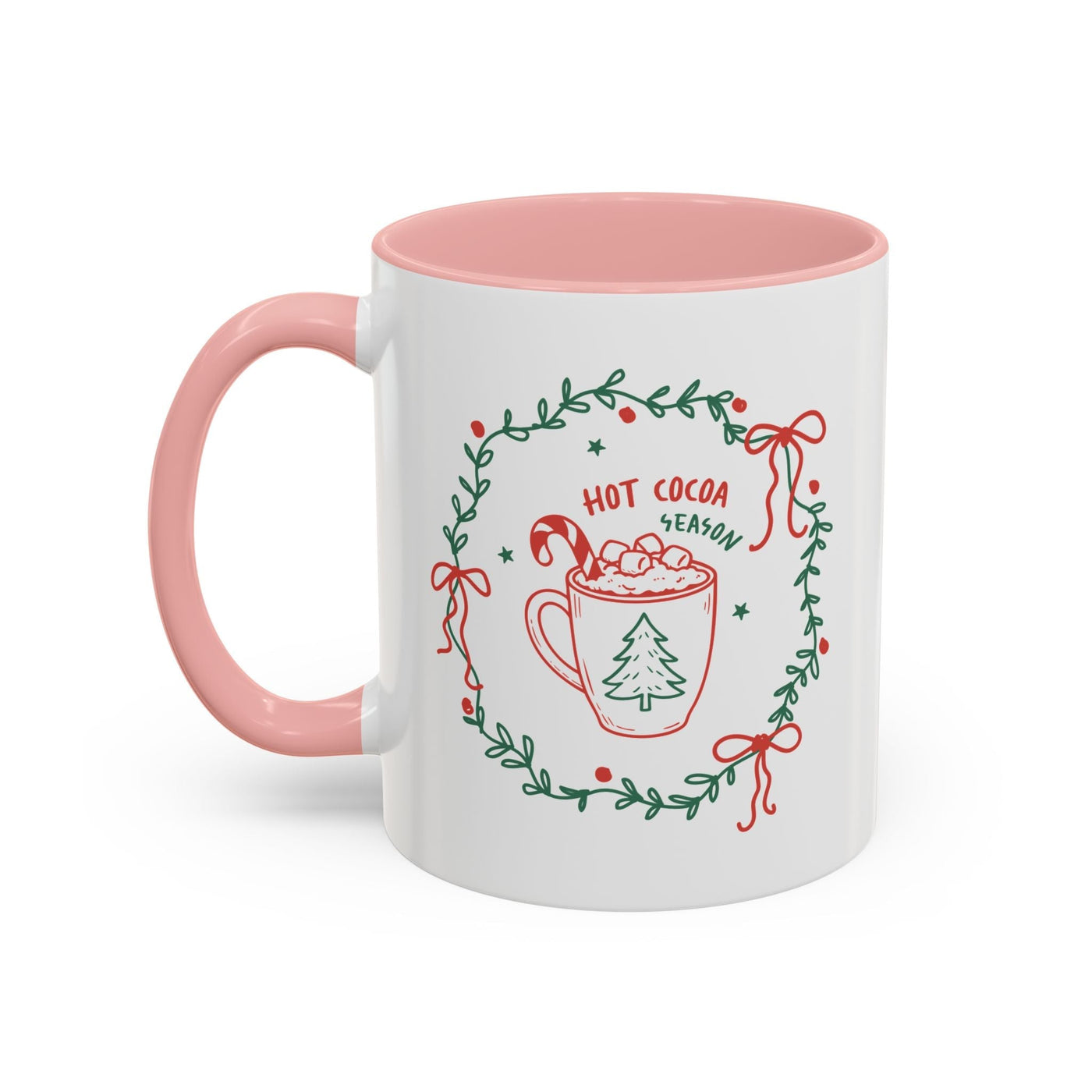 White ceramic mug with pink handle and interior featuring hot cocoa season design and greenery wreath