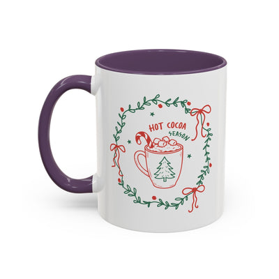 White ceramic mug with purple handle and interior, festive hot cocoa season design with greenery wreath and red bows