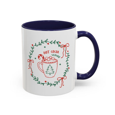 white ceramic mug with blue interior and handle featuring hot cocoa season design with festive wreath and candy cane illustration