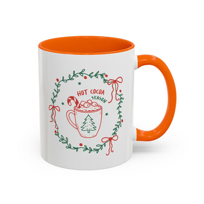 white ceramic mug with orange interior and handle featuring hot cocoa season design and holiday greenery wreath
