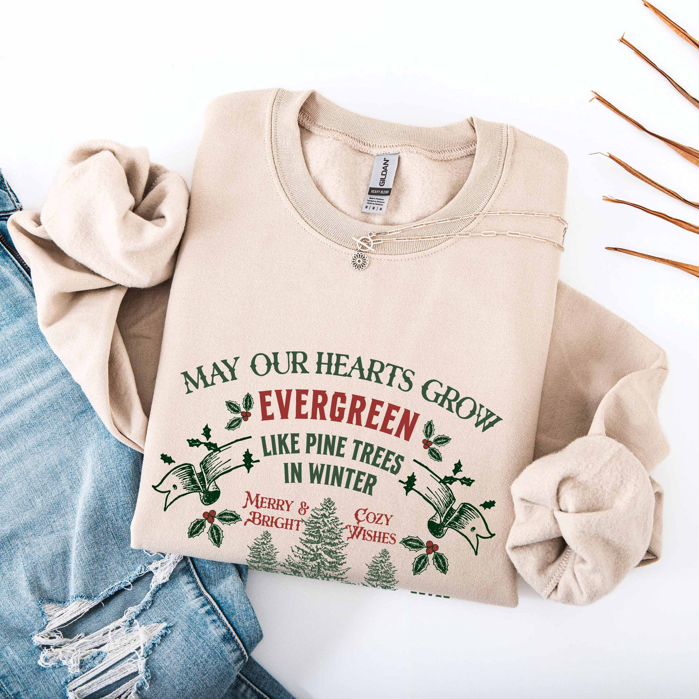Beige Christmas crewneck sweatshirt with festive holiday text and evergreen tree design, styled with ripped denim jeans and a necklace.