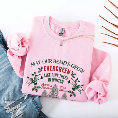 Pink Christmas Crewneck sweatshirt with green and red holiday text and pine tree design, paired with denim jeans and a necklace on white background