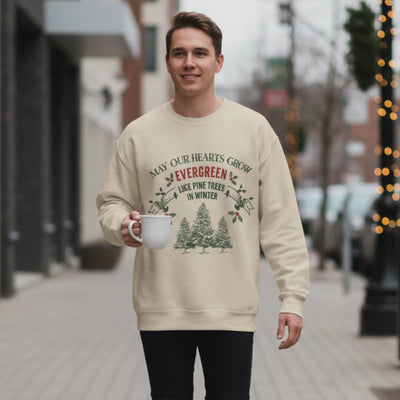Man wearing beige Christmas Crewneck sweatshirt with green holiday tree design and holding a white mug outdoors on city street