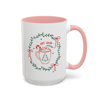 white ceramic mug with pink handle and interior featuring hot cocoa season wreath design