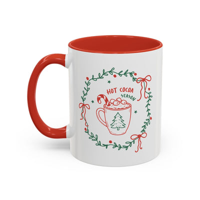 White ceramic mug with red interior and handle featuring a Cozy Hot Cocoa Season festive design with greenery wreath.