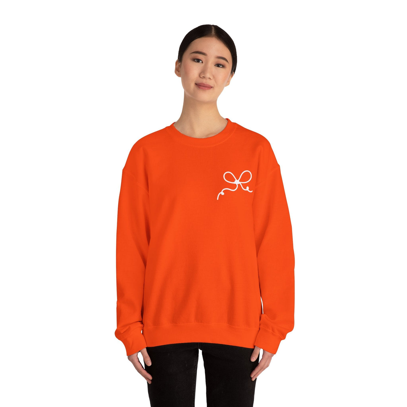 Woman wearing bright orange Coquette Bow crewneck sweatshirt with small white bow design on chest
